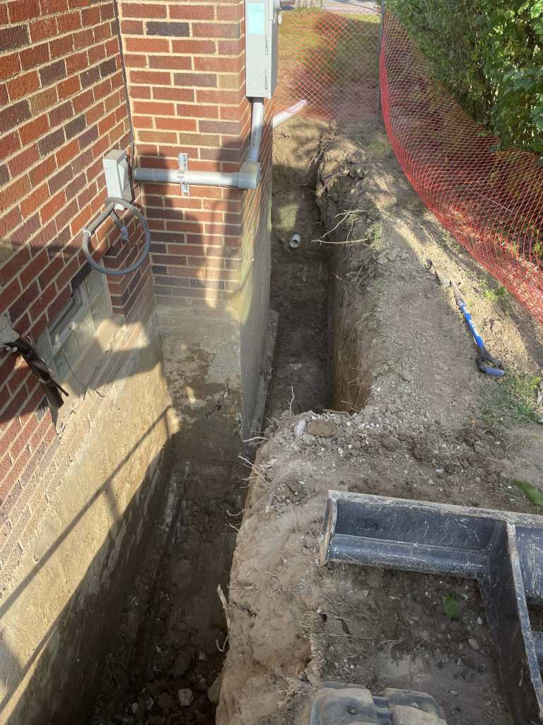 Excavated trench beside brick building