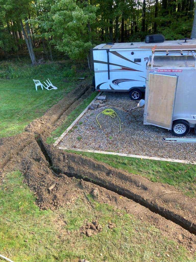 Excavated trench beside parked trailers.